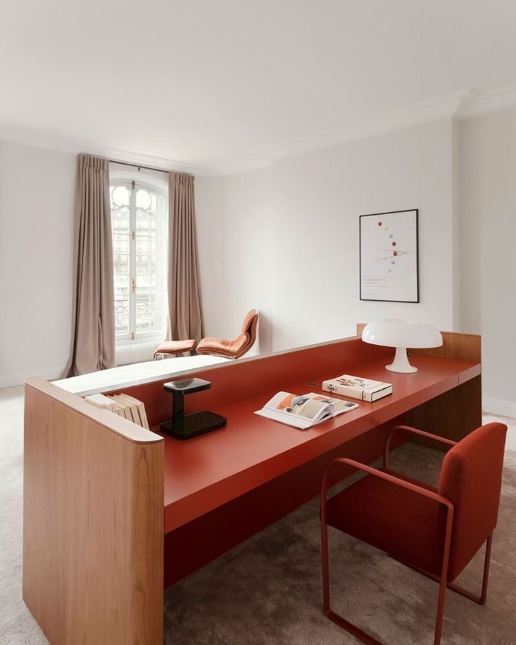 Red-lacquered desk by a tall window with a mushroom lamp and an armchair.